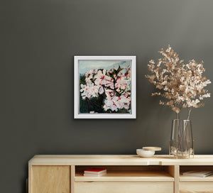 An expressive and lively painting of wild plum blossoms hangs on a dark grey wall beside a vase of dried flowers that sits on a sideboard.